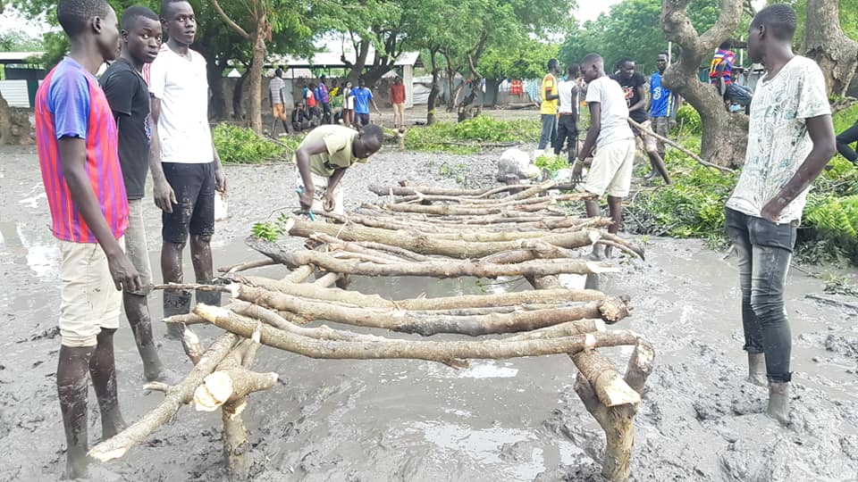 Student stand alongside the bridge that is still in progress. the bridge is built from sticks and logs
