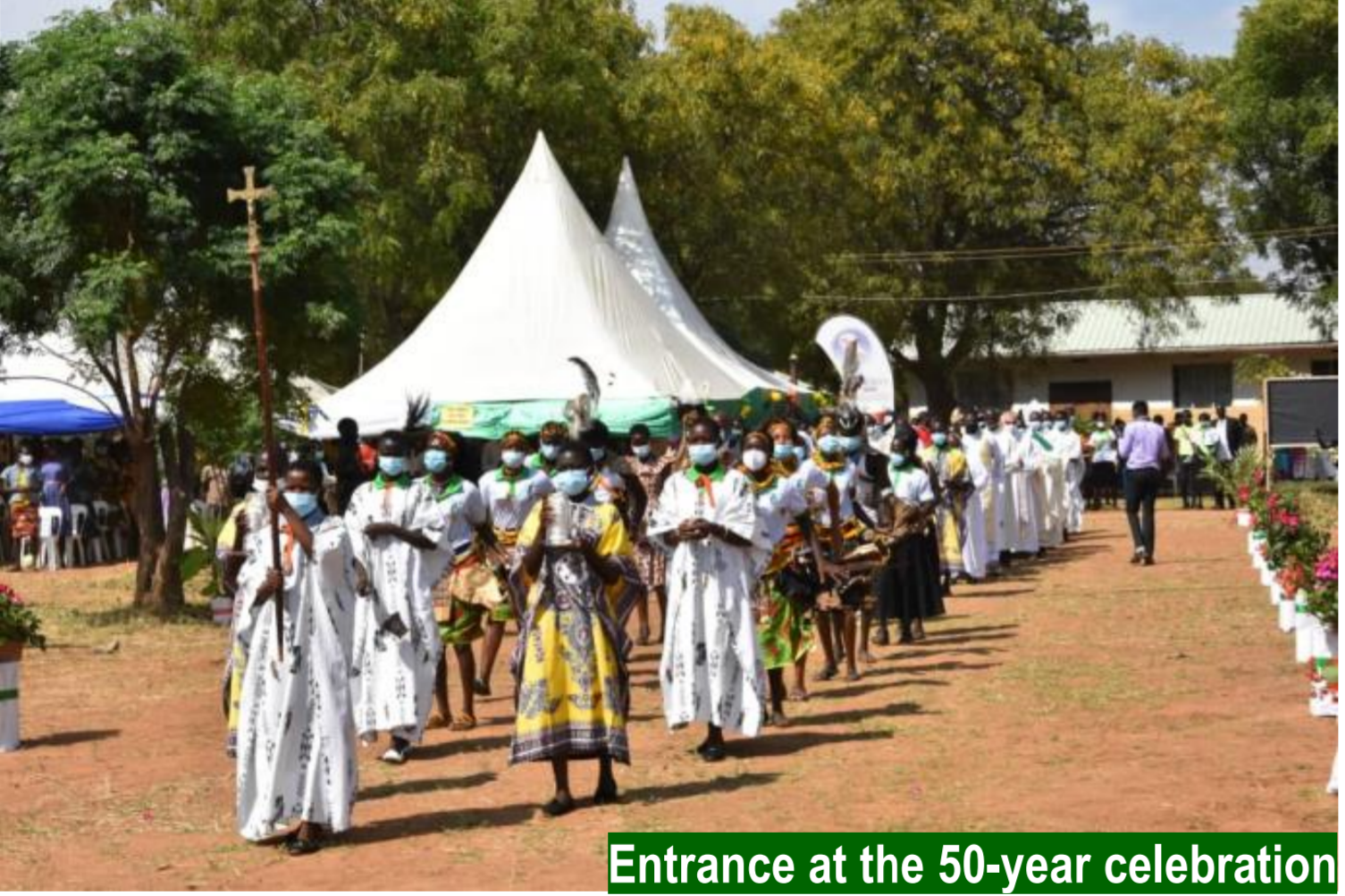 young people process down  a dusty path in the hospital courtyard as they celebrate St Kizito Hospitals anniversary