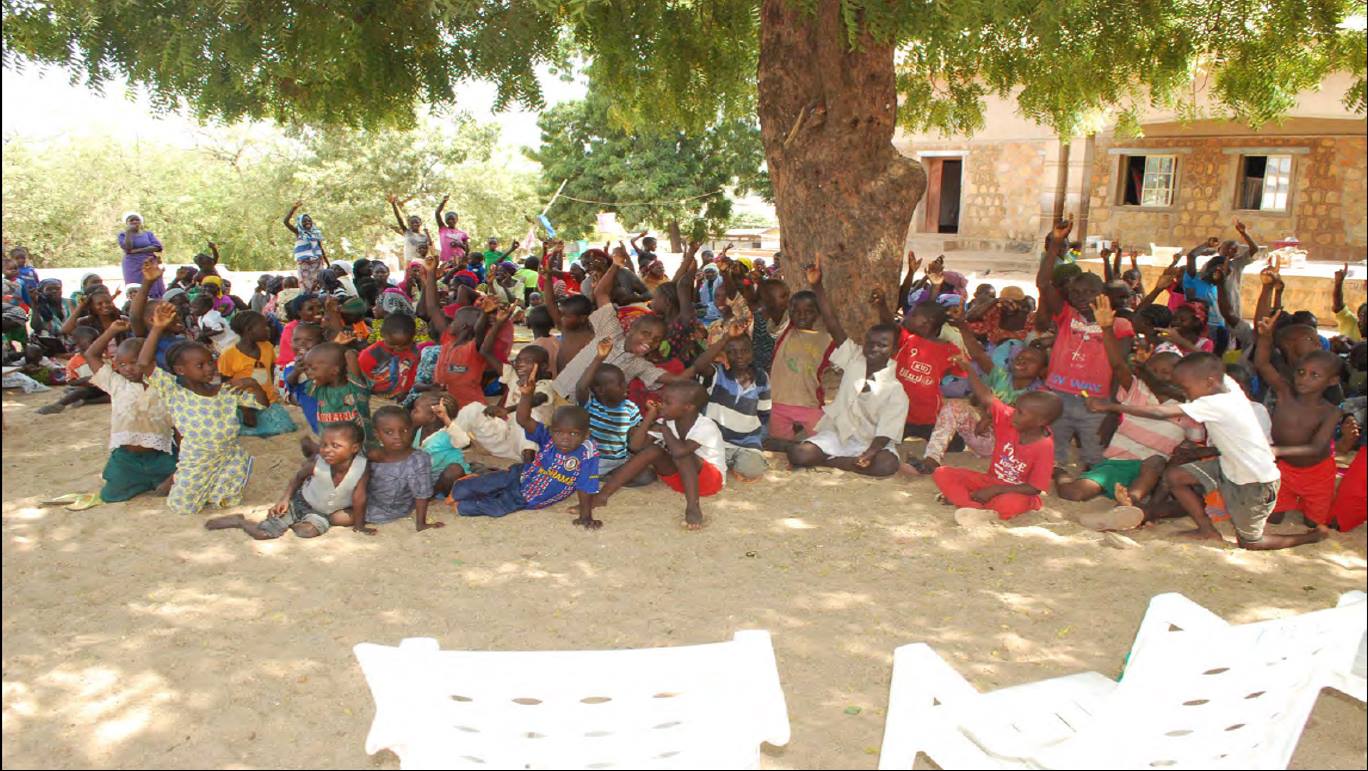 a large group of African children sits in the shade of a mango tree they are from the ST Theresa IDP Camp in Yola