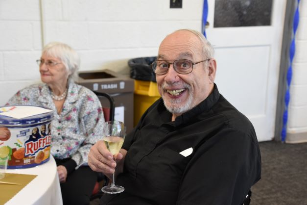 Fr Tom Vermiglio smiles broadly holing a flute of champaign to celebrate his 50th ordination anniversary