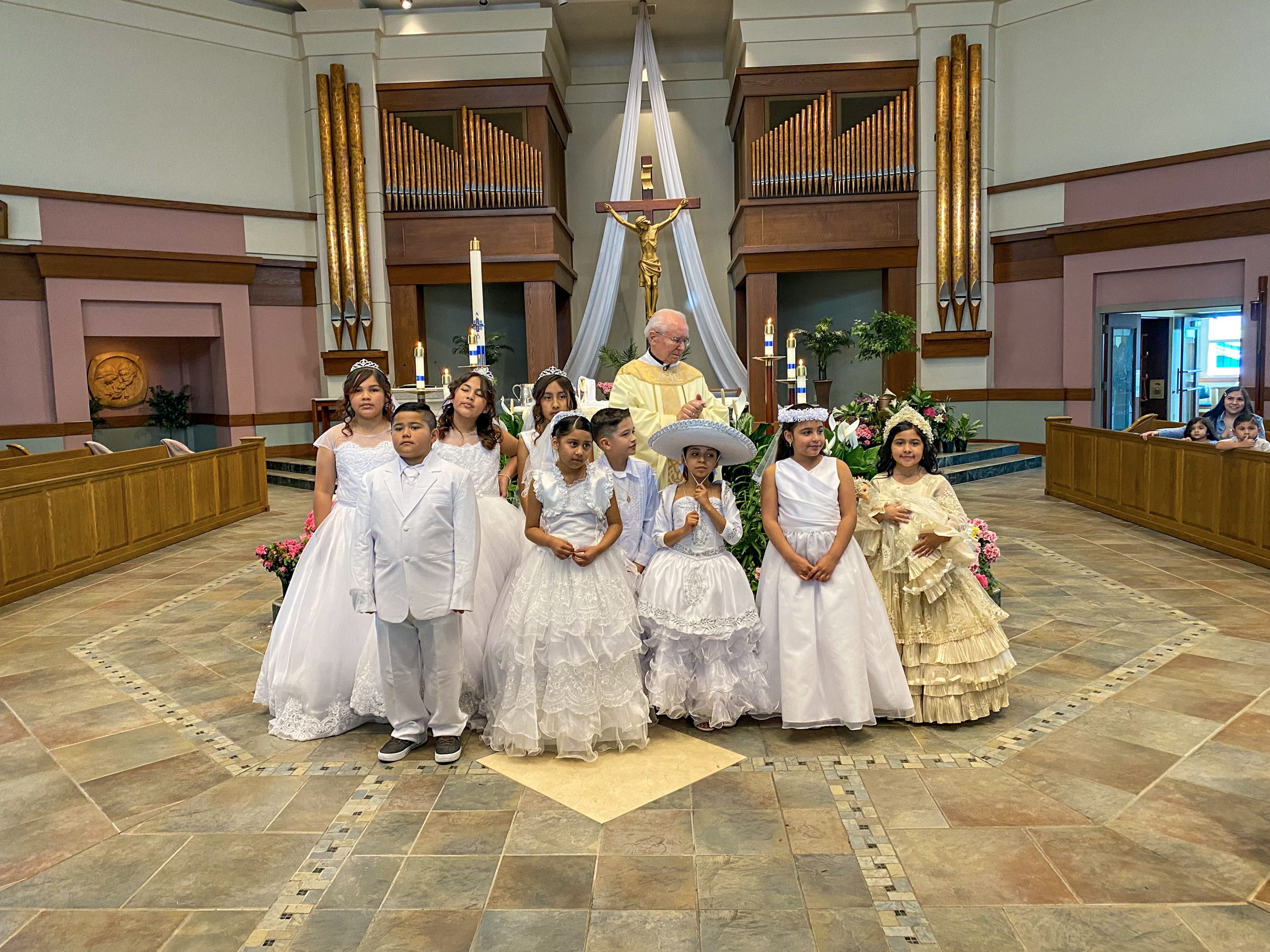 Fr Louie stands with a group of first communicants all dressed in their white dresses and suits.