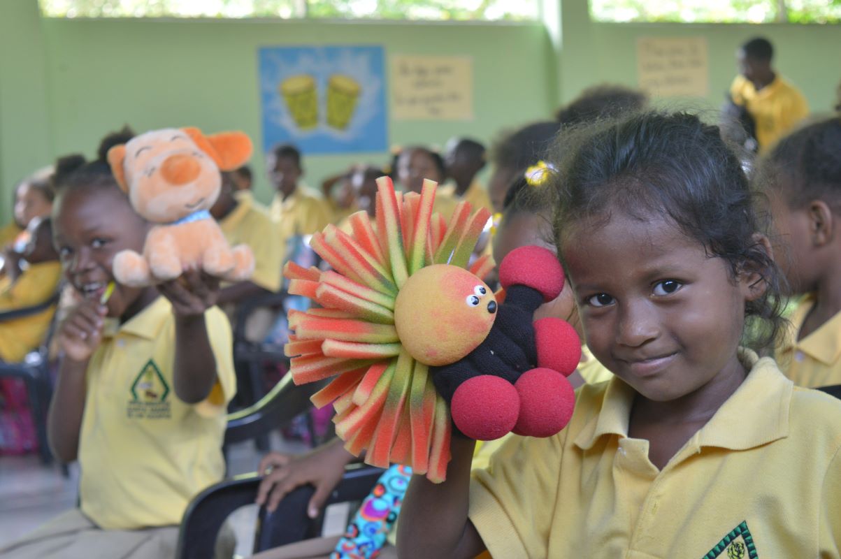 A young girl at Santa María de los Cayapas Fiscal Unit holds a hand puppet and smiles brightly at the camera